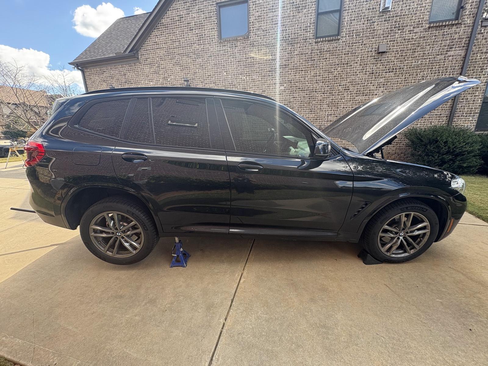 Black SUV on jack stands in a home driveway with the hood up