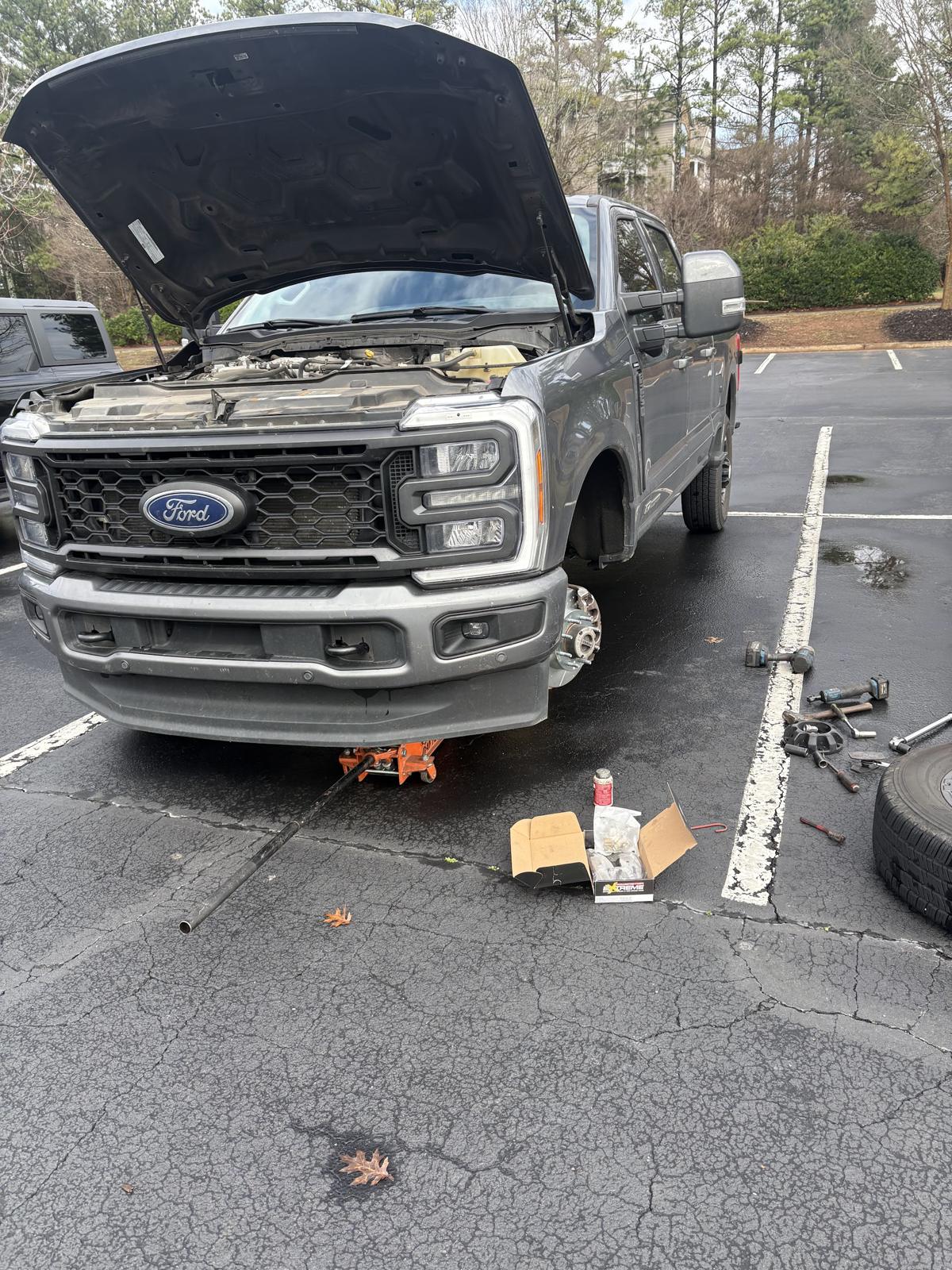 Ford pickup with the hood up and a front wheel off in a parking lot