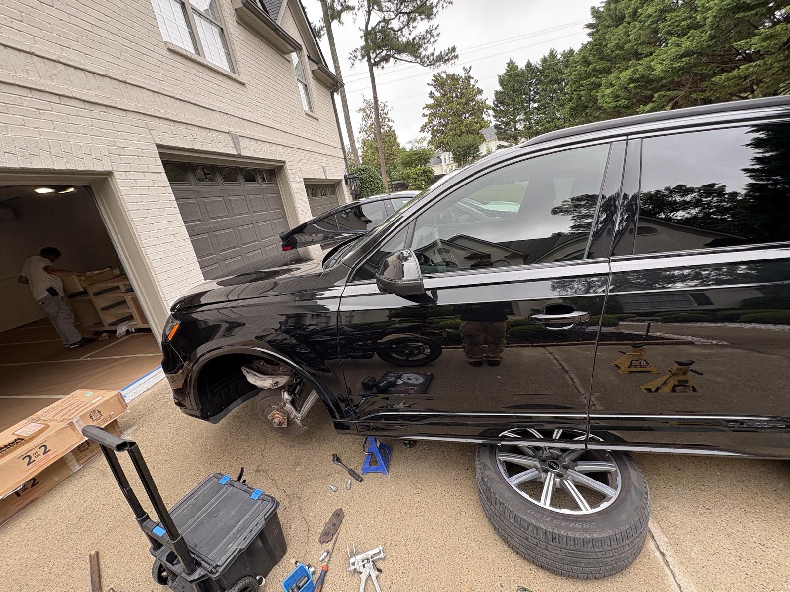 Black SUV with a rear wheel off outside a garage